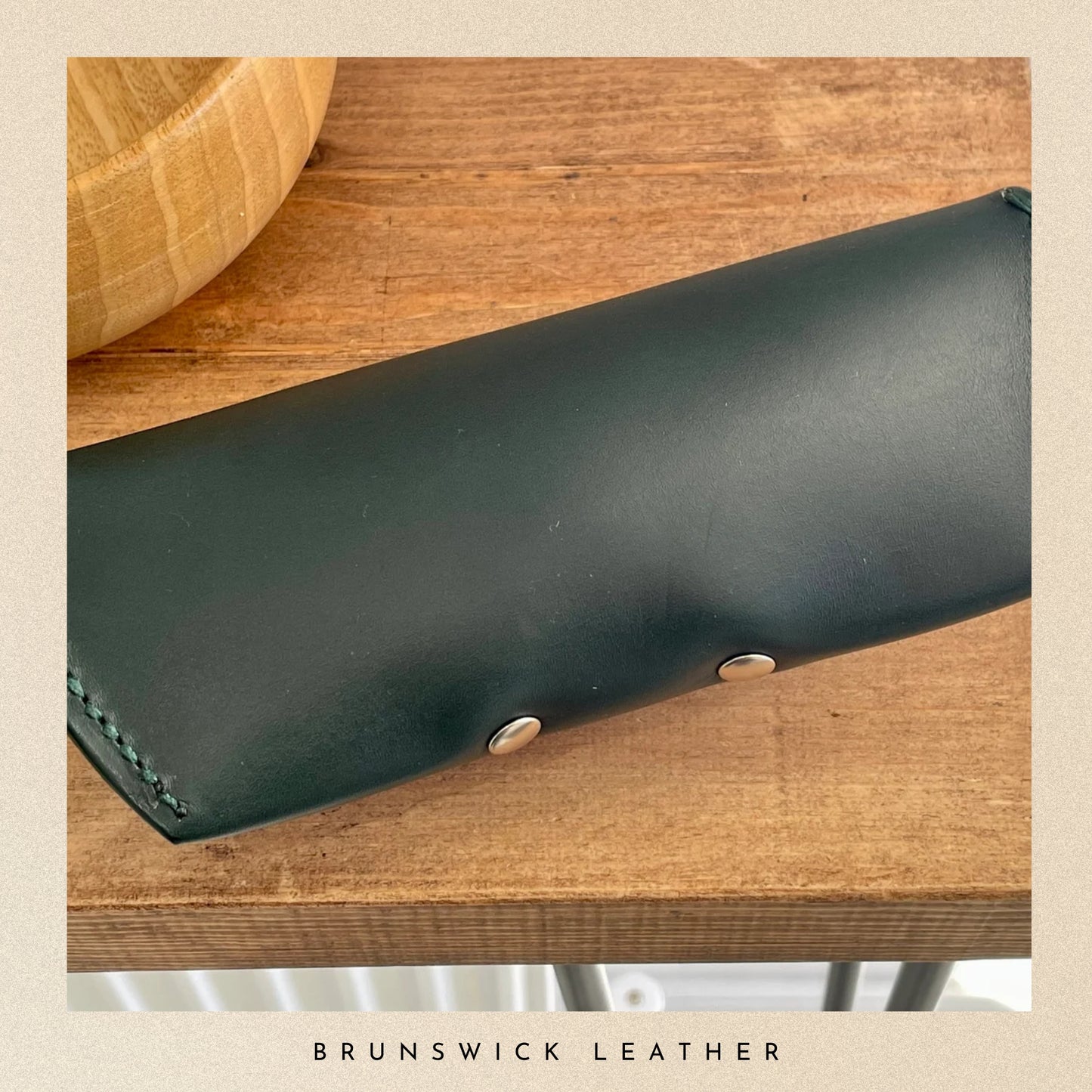 Black leather wallet on a wooden surface with 'Brunswick Leather' branding.