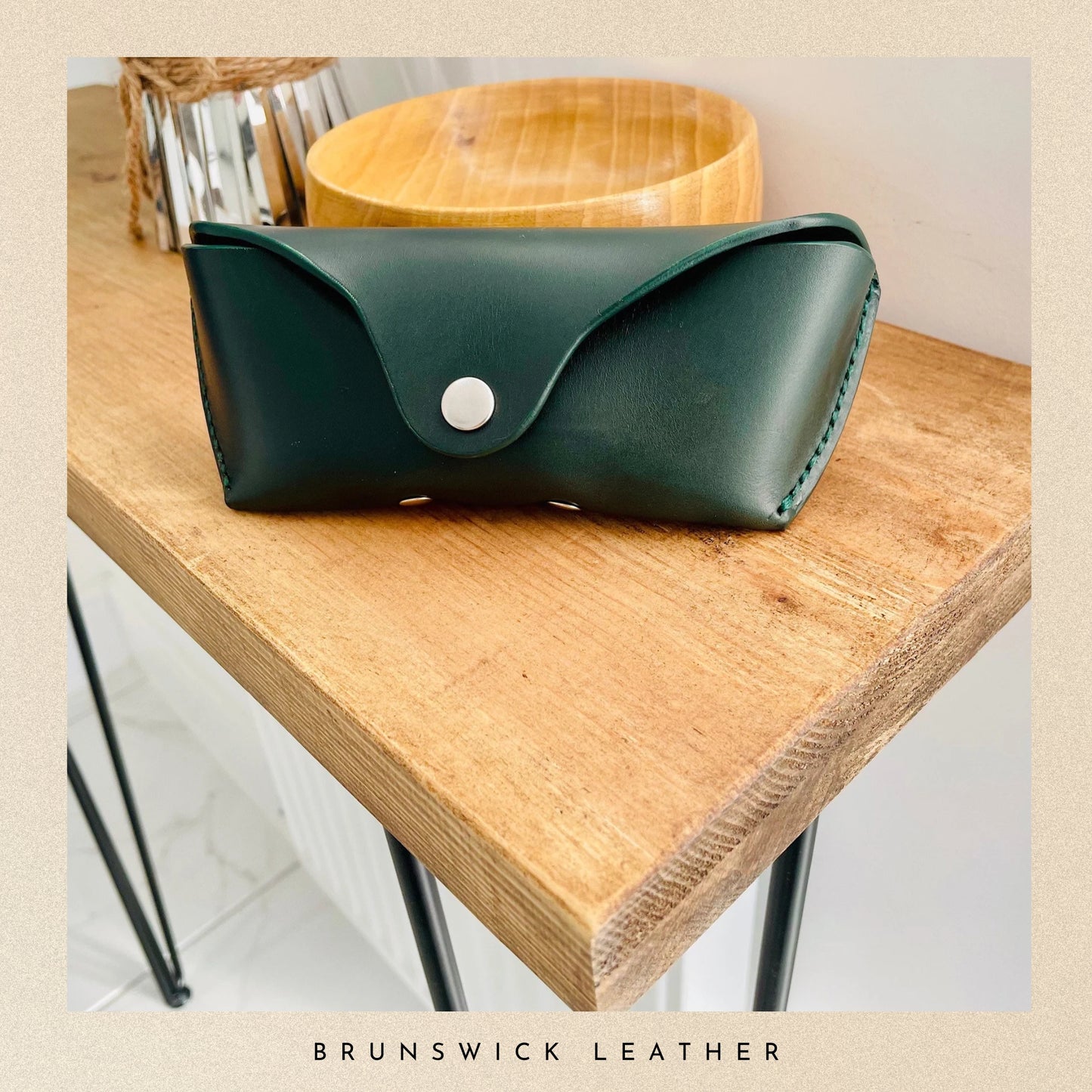 Green leather pouch with a silver button on a wooden surface, branded 'Brunswick Leather'.