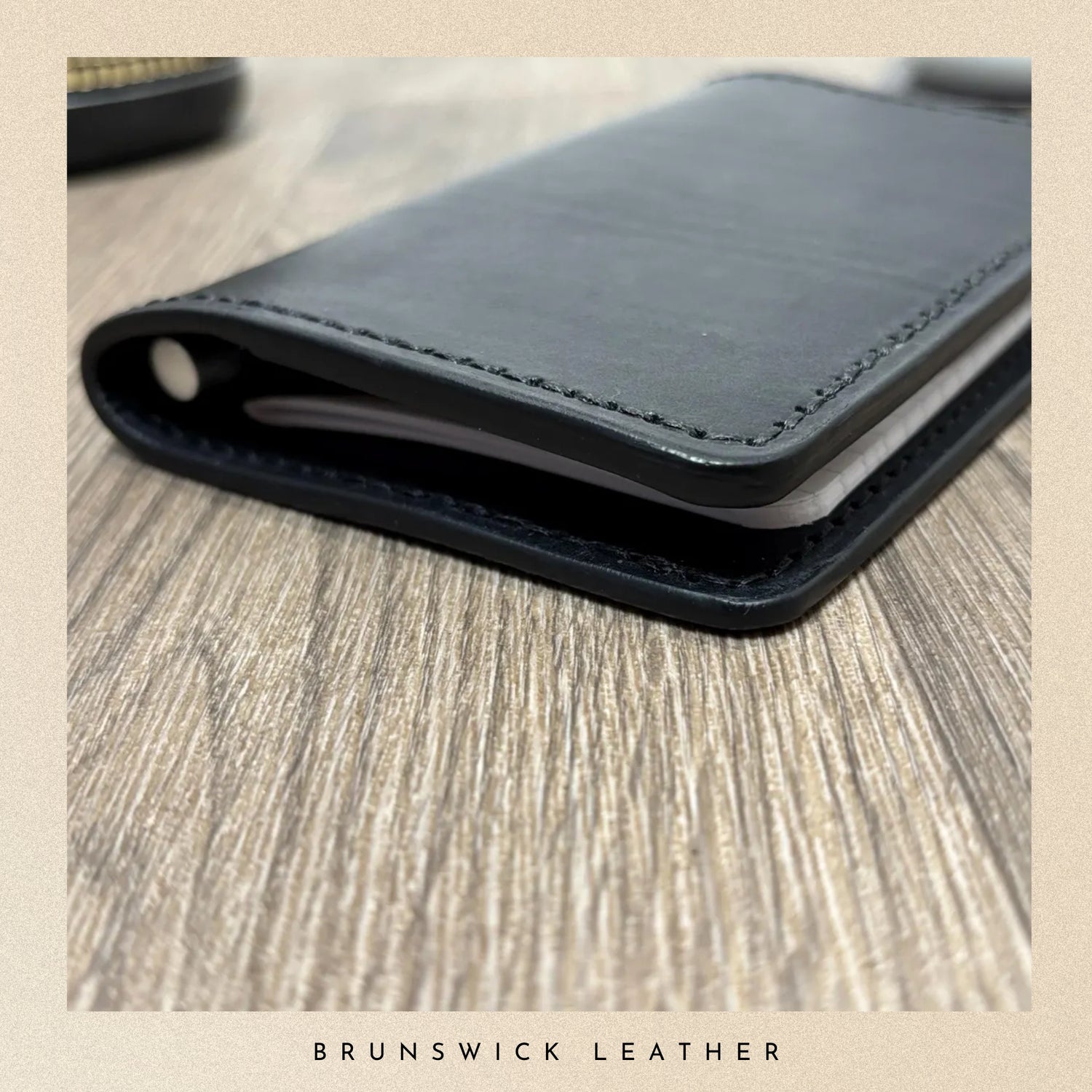 Black leather wallet on a wooden surface with 'Brunswick Leather' branding.