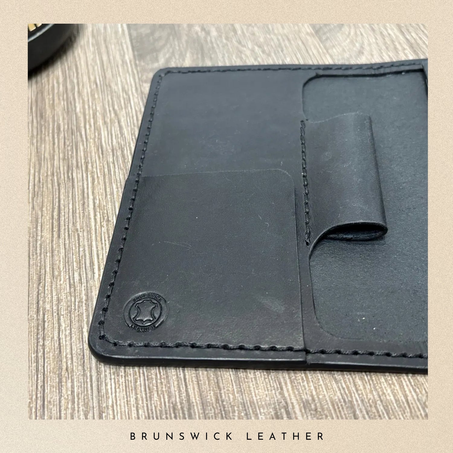 Black leather wallet with visible stitching on a wooden surface, branded 'Brunswick Leather'.