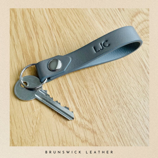 Gray leather keychain with keys on a wooden surface, branded 'LJC'.