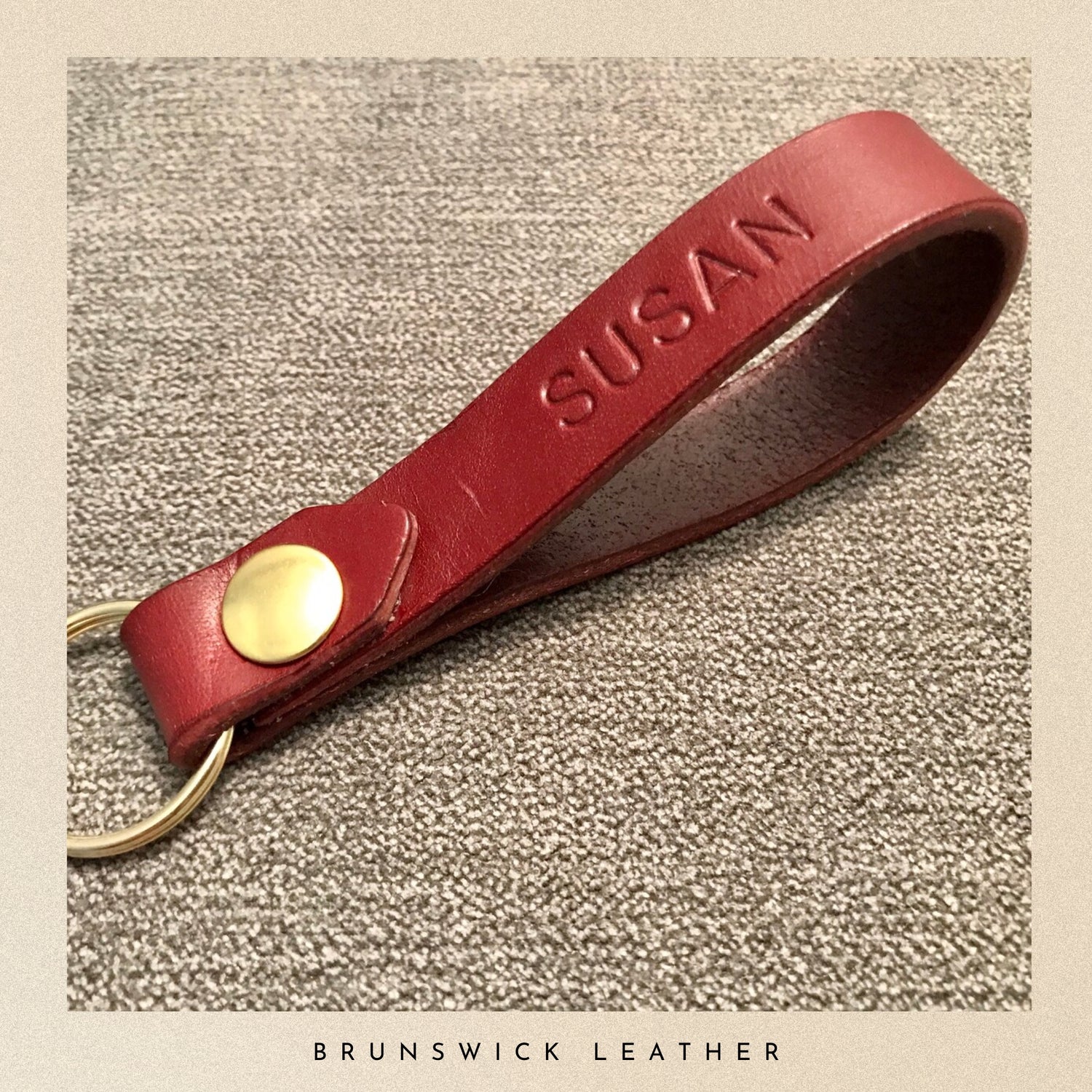 Burgundy leather keychain with 'SUSAN' engraving on a textured beige background, branded 'Brunswick Leather'.