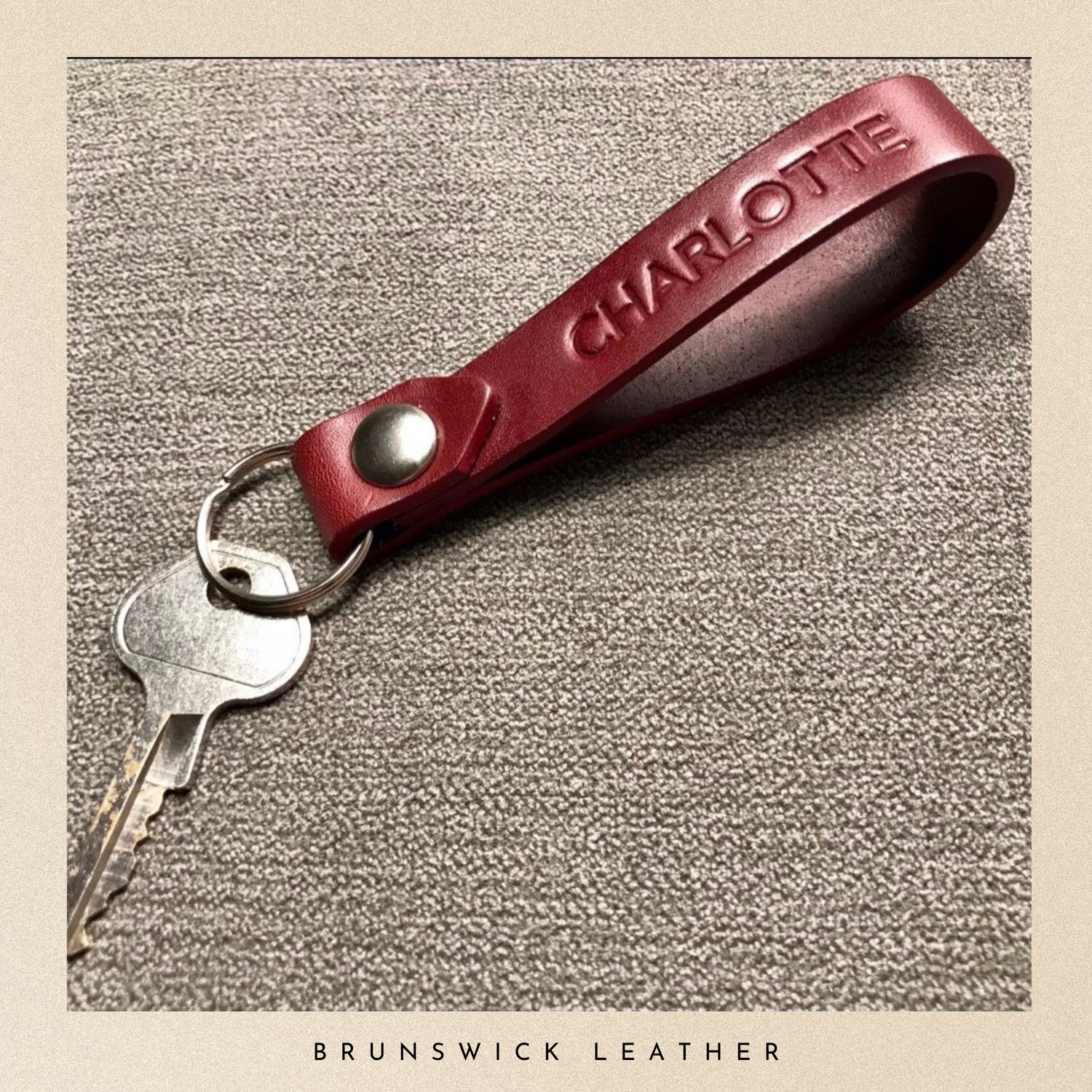 Burgundy leather key fob with 'Charlotte' engraving on a textured surface, branded 'Brunswick Leather'.