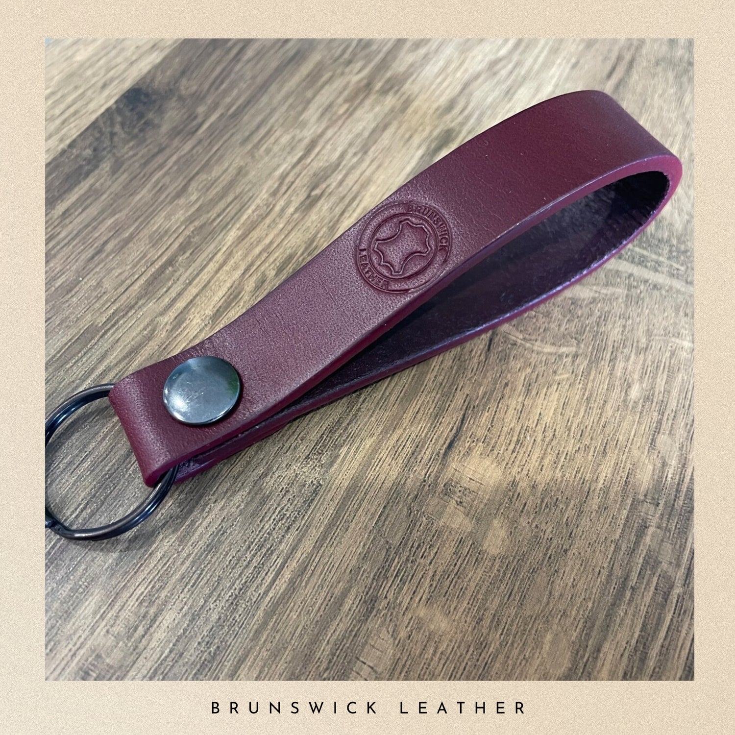 Burgundy leather keychain with a metal ring on a wooden surface, branded 'Brunswick Leather'.