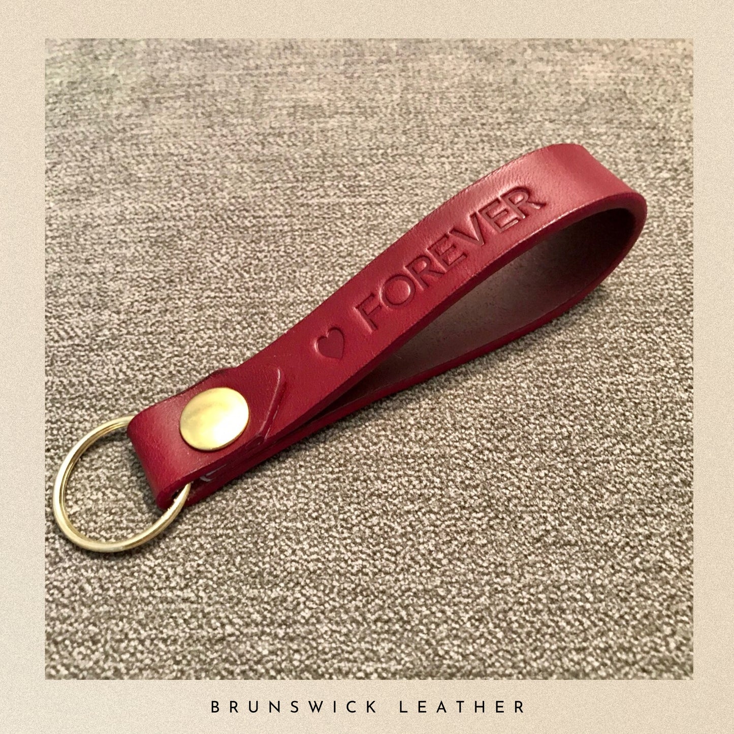 Burgundy leather keychain with 'FOREVER' engraving on a textured beige background, branded 'Brunswick Leather'.