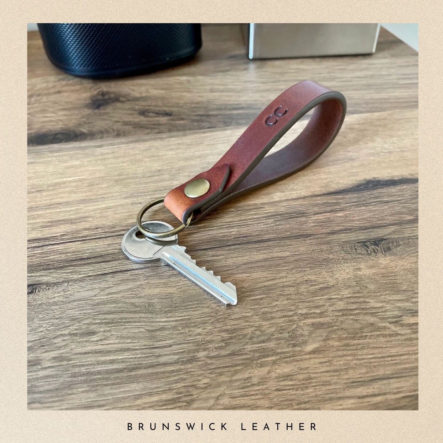 Brown leather keychain with a key on a wooden surface, branded 'Brunswick Leather'.