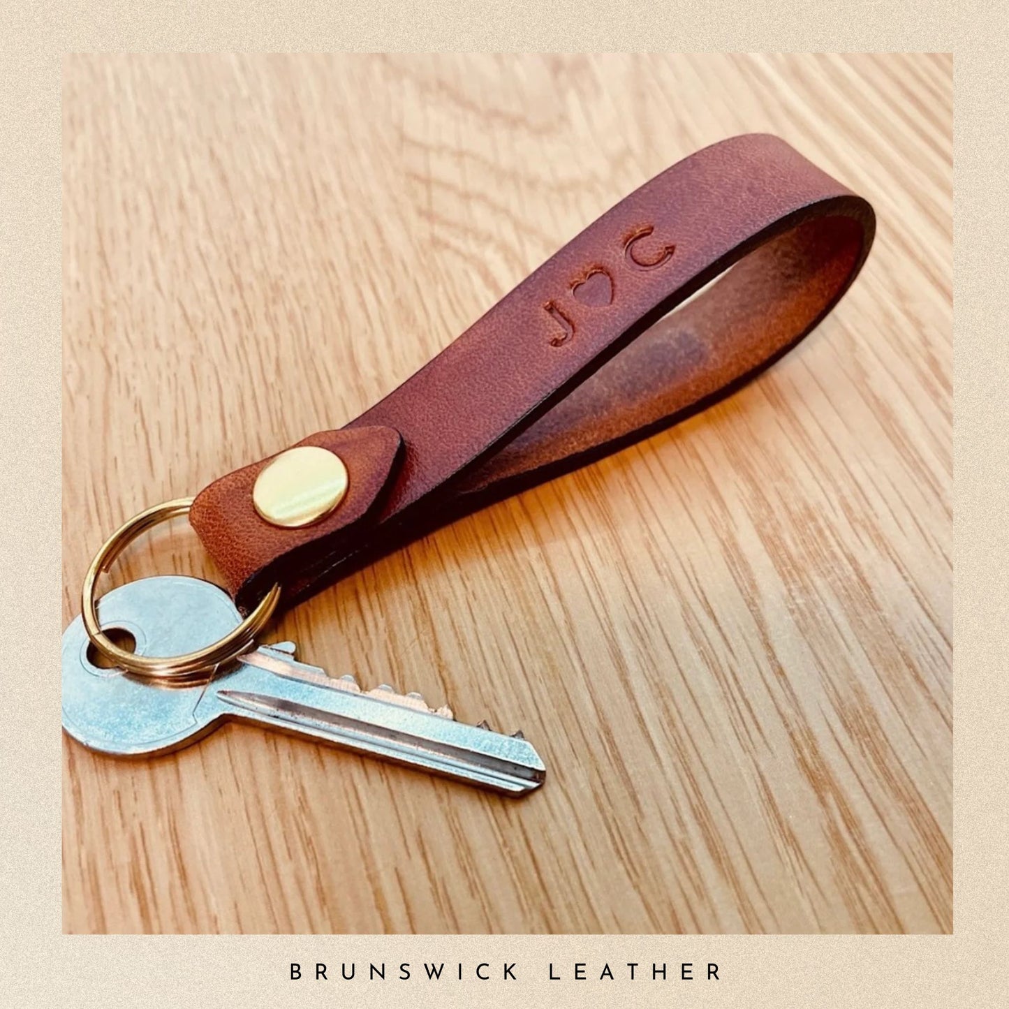 Brown leather keychain with keys on a wooden surface, branded 'Brunswick Leather'.