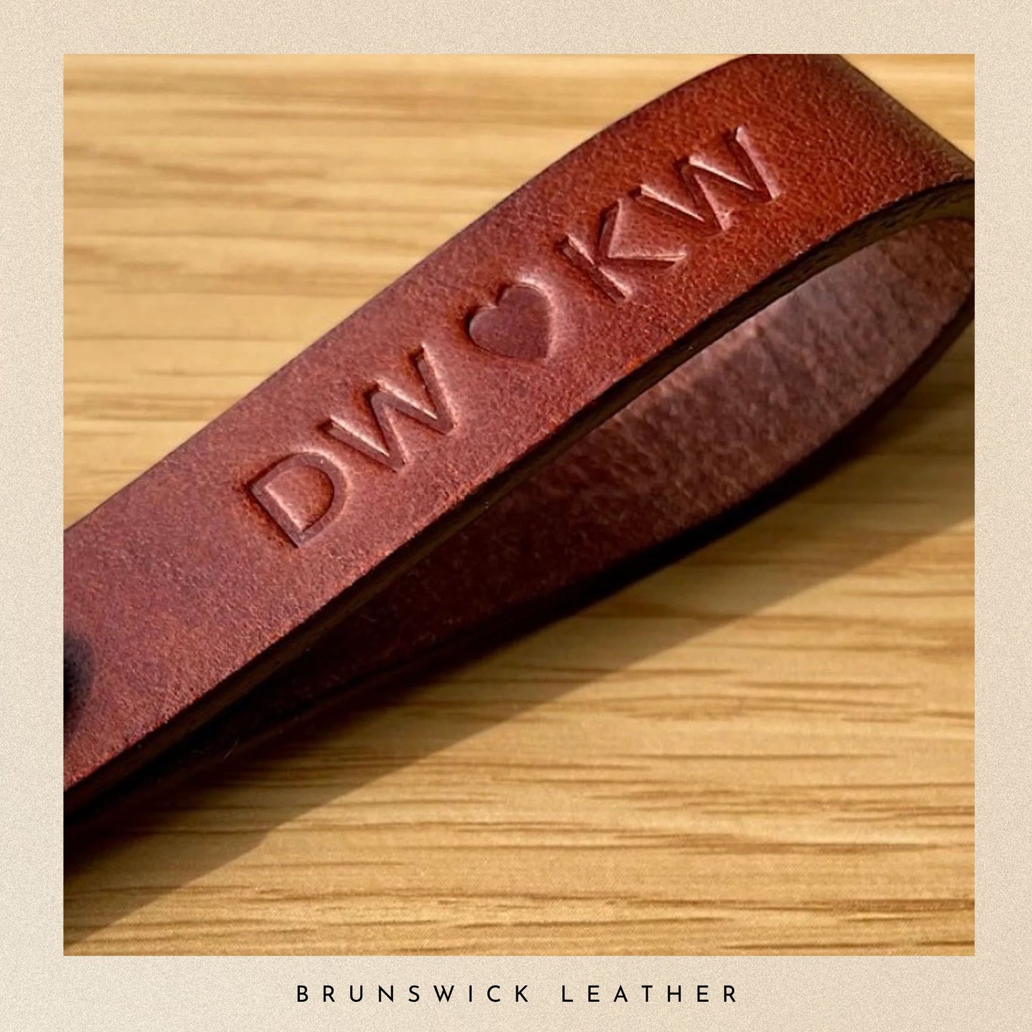Brown leather strap with embossed initials on a wooden surface, branded 'Brunswick Leather'.