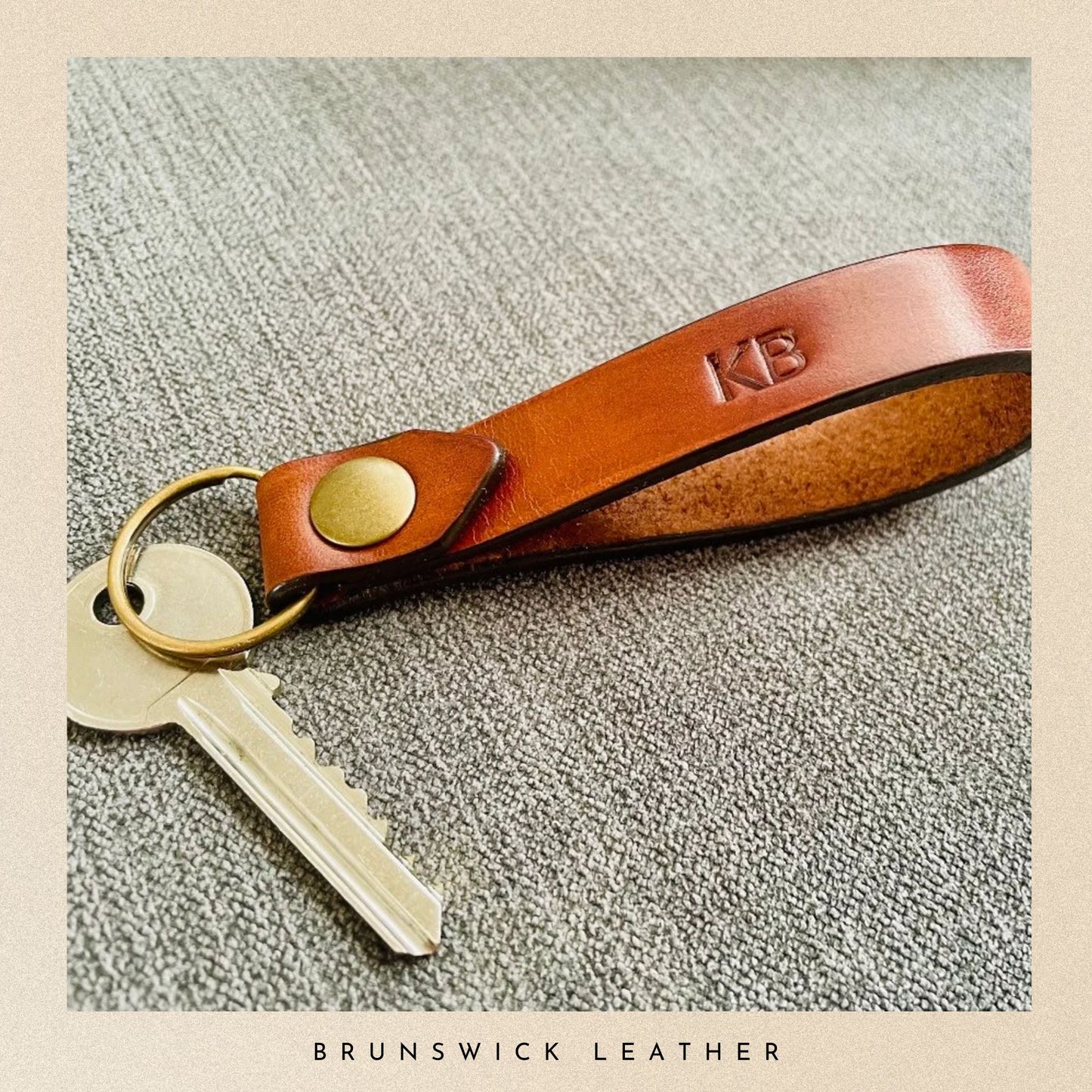 Brown leather keychain with keys on a textured surface, branded 'Brunswick Leather'.