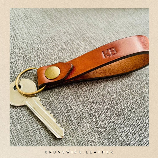 Brown leather keychain with keys on a textured surface, branded 'Brunswick Leather'.