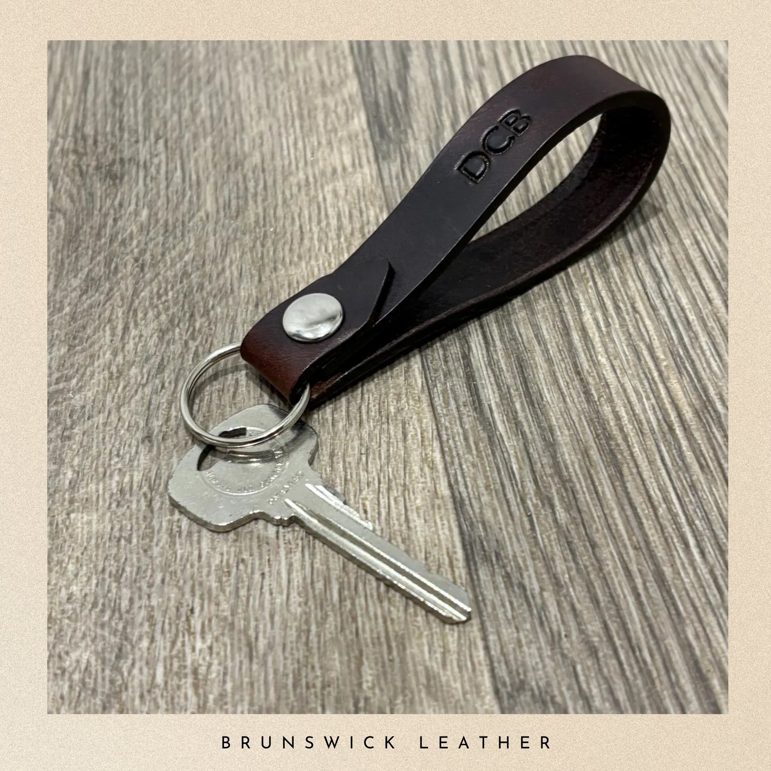 Brown leather keychain with silver key on a wooden surface, branded 'Brunswick Leather'.