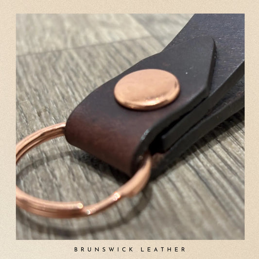 Leather key fob with copper accents on a wooden surface, branded 'Brunswick Leather'.