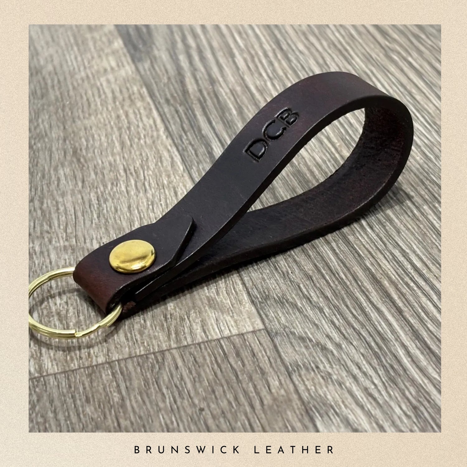 Brown leather keychain with gold accent on a wooden surface, branded 'DCB'.