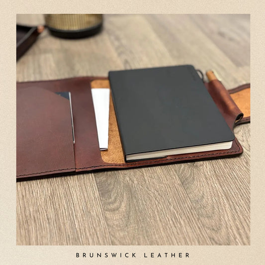 Leather-bound notebooks on a wooden surface with 'Brunswick Leather' branding.