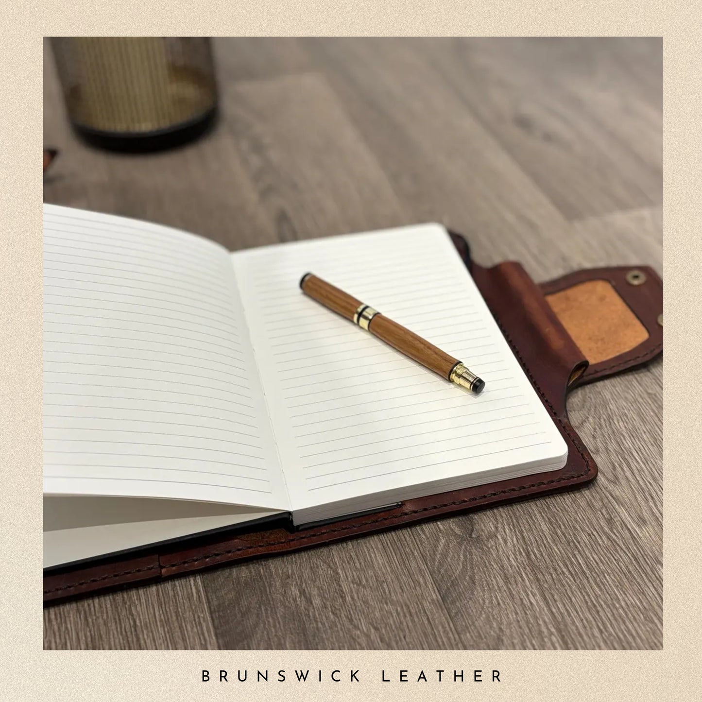 Open notebook with a wooden pen on a wooden surface, featuring Brunswick Leather branding.