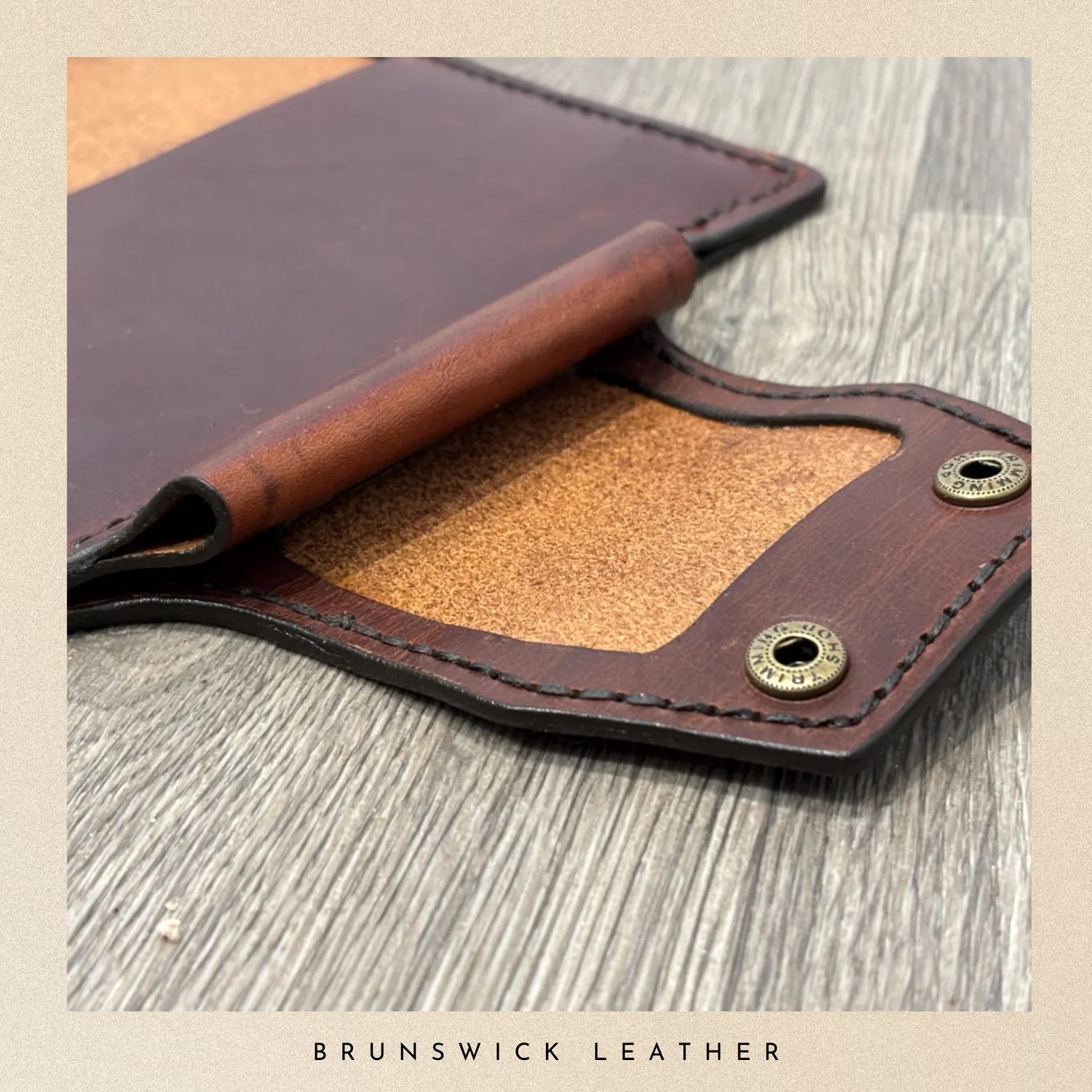 Brown leather wallet with gold rivets on a wooden surface, featuring 'Brunswick Leather' branding.