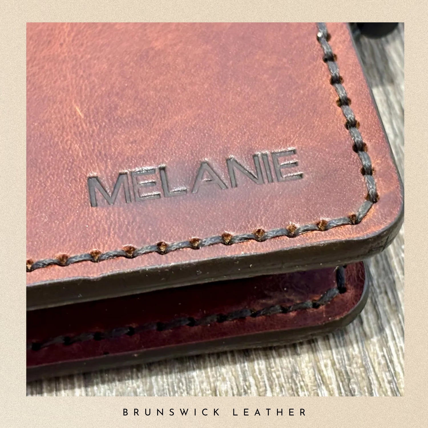 Brown leather wallet with 'Melanie' engraving on a wooden surface, branded 'Brunswick Leather'.