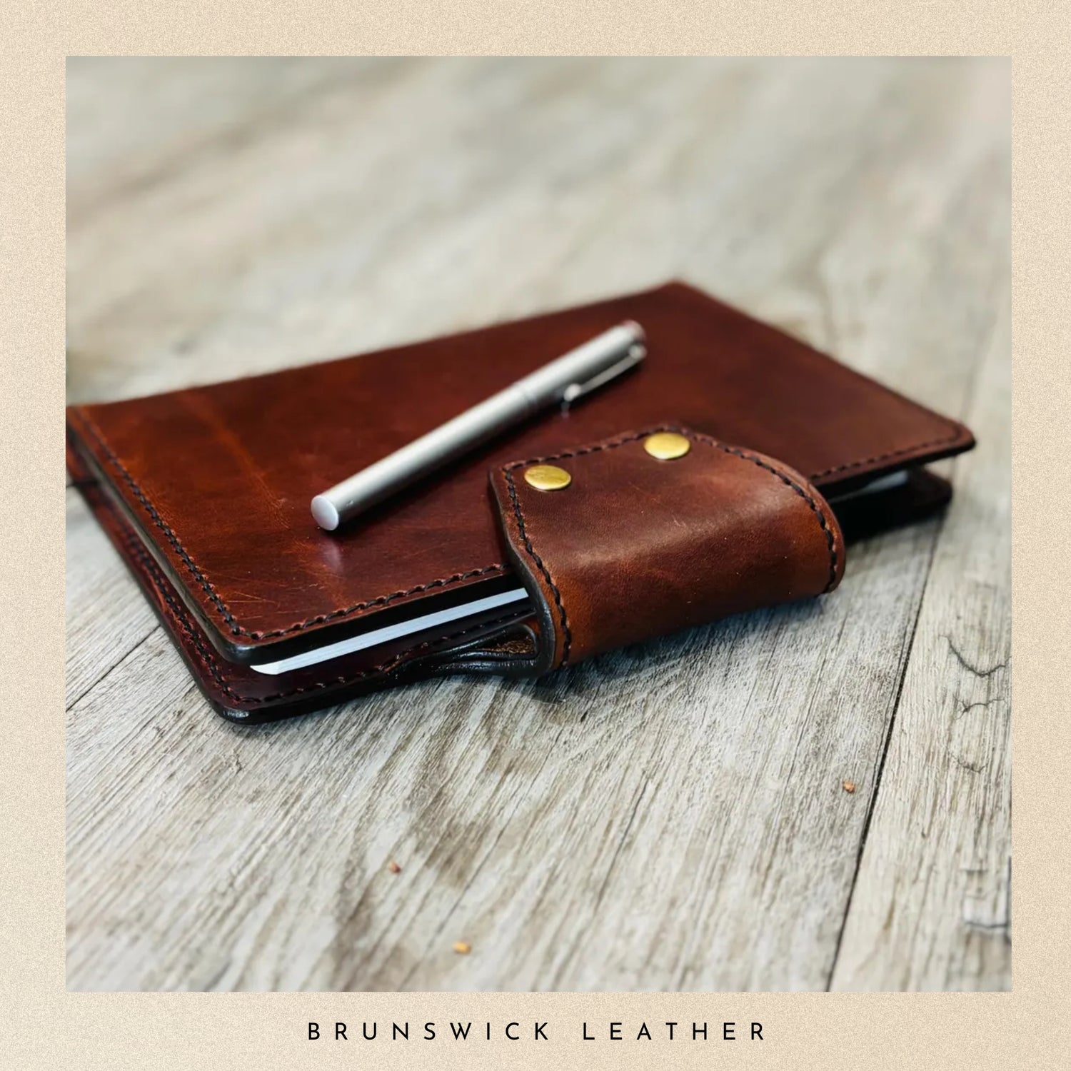 Brown leather wallet with a pen on a wooden surface, branded 'Brunswick Leather'.