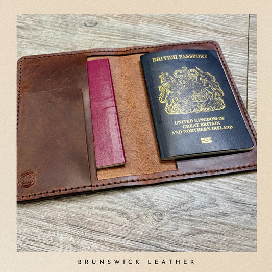 Brown leather wallet with passport and pink card on a wooden surface, branded 'Brunswick Leather'.