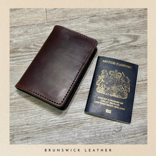 Brown leather passport holder next to a British passport on a wooden surface, with 'Brunswick Leather' branding.