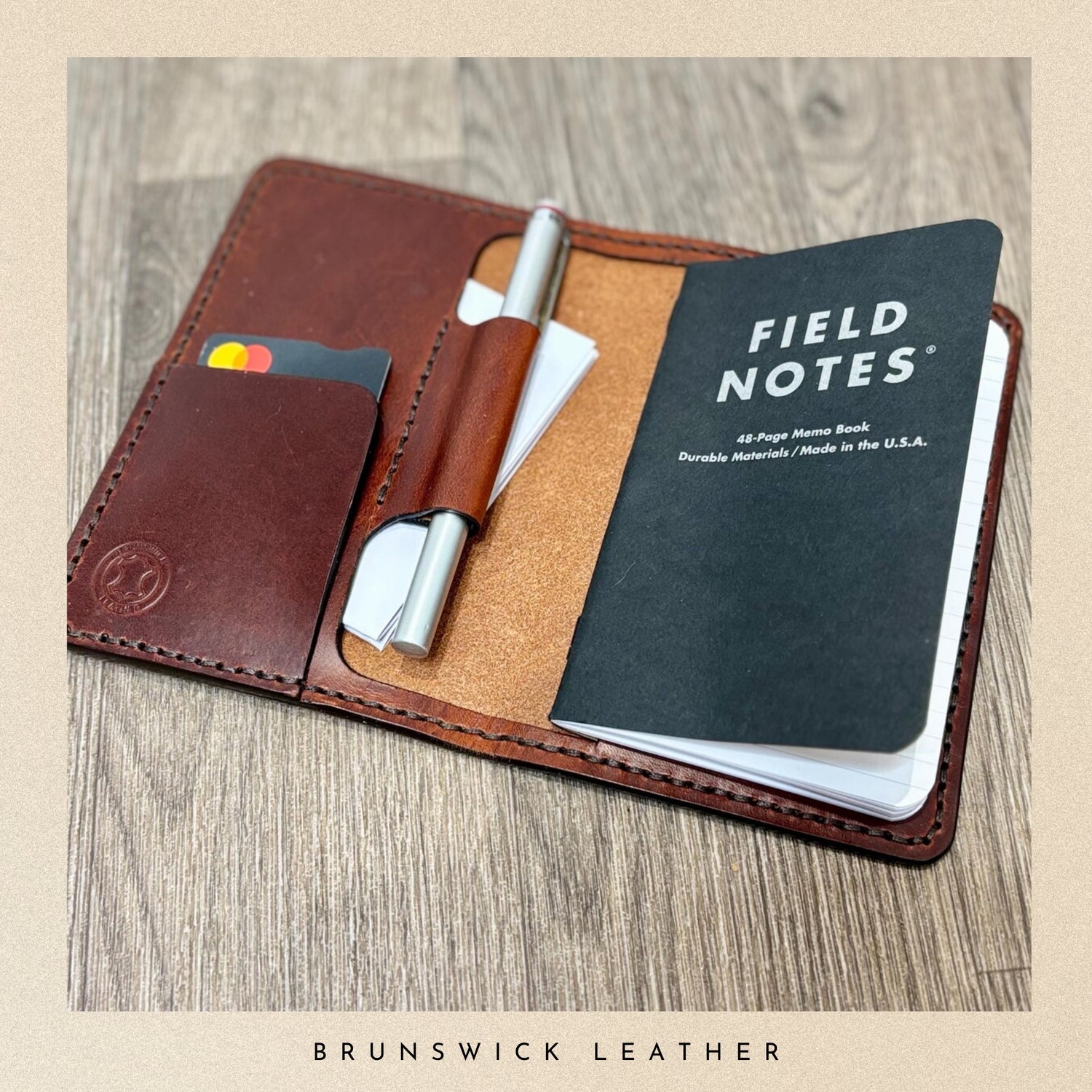 Brown leather wallet with a pen, cardholder, and Field Notes notebook on a wooden surface.