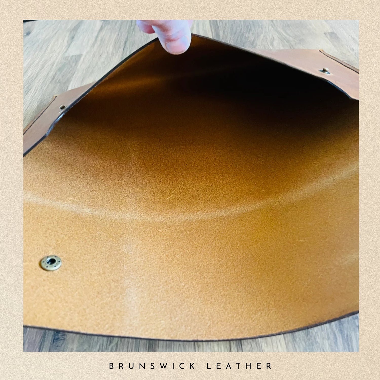 Close-up of a brown leather surface with a hand holding it, on a wooden floor.