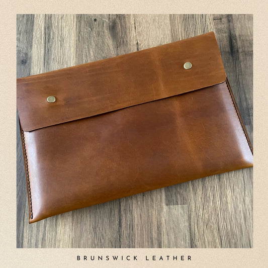Brown leather clutch on a wooden surface with 'Brunswick Leather' branding.