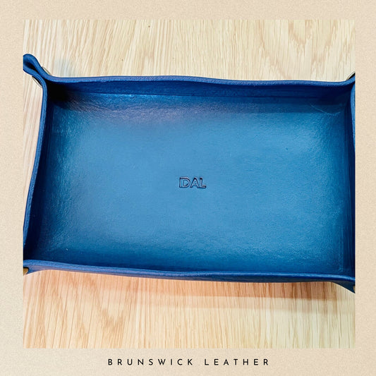 Blue leather tray with 'DAL' branding on a wooden surface, featuring 'Brunswick Leather' branding at the bottom.