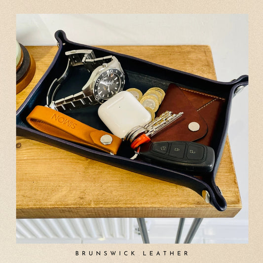 Tray with assorted items including a watch, keys, and phone case on a wooden surface with 'Brunswick Leather' branding.