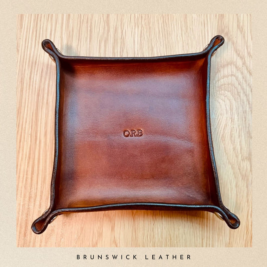 Brown leather tray with 'ORB' engraving on a wooden surface, branded 'Brunswick Leather'.