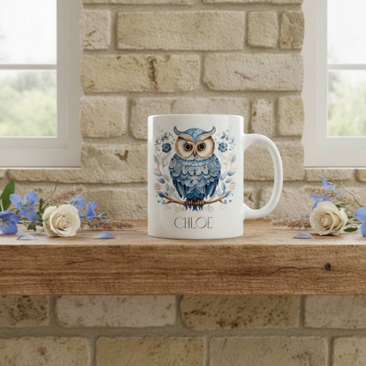 White mug with an owl design and 'Chloe' text on a wooden surface with flowers and a stone wall background