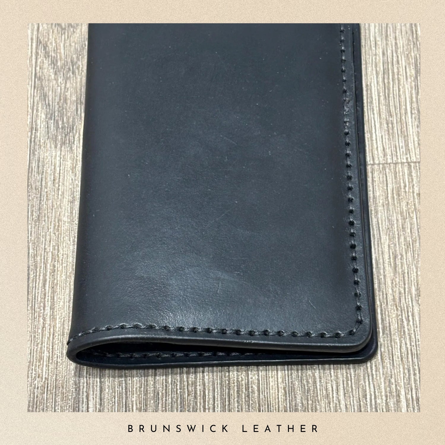 Black leather wallet on a wooden surface with 'Brunswick Leather' branding.
