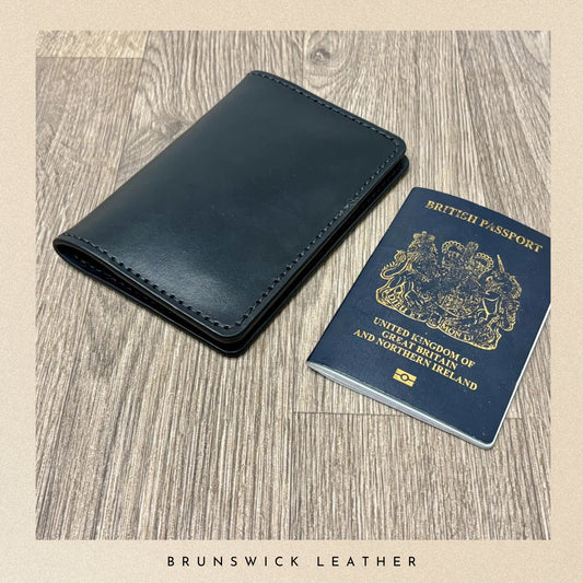 Blue leather wallet and British passport on a wooden surface with 'Brunswick Leather' branding.