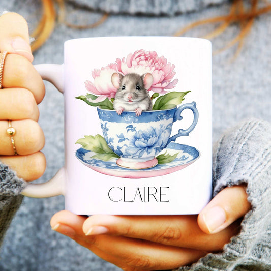 Person holding a mug with a mouse in a teacup design and 'CLAIRE' branding.