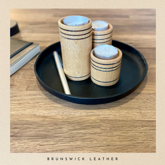 Wooden candles with striped design on a black leather tray on a wooden surface, branded 'Brunswick Leather'.