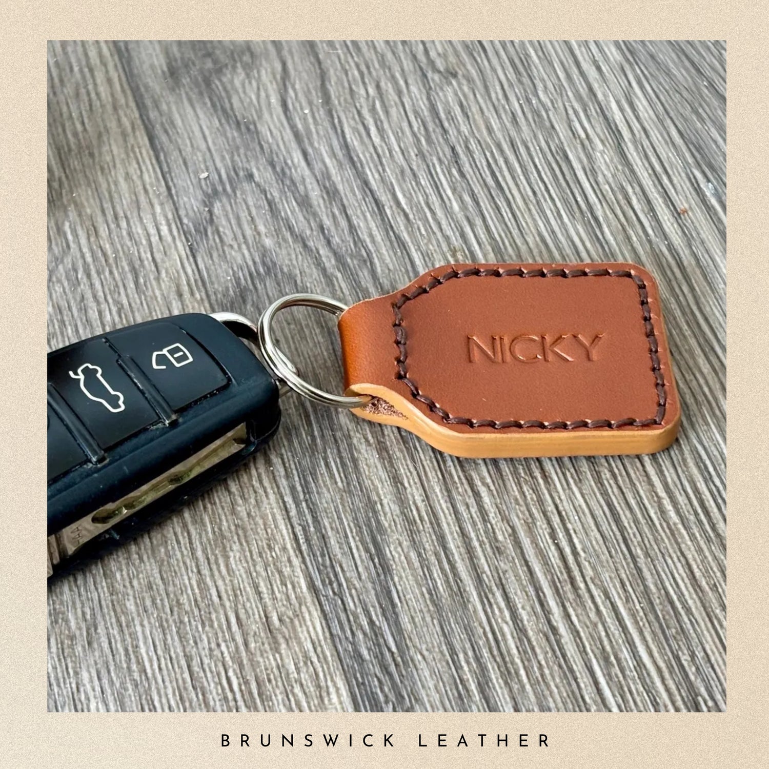 Brown leather keychain with 'NICKY' engraving attached to a car key on a wooden surface, branded 'Brunswick Leather'.