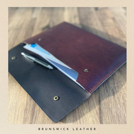 Leather wallet with pen on a wooden surface, branded 'Brunswick Leather'.