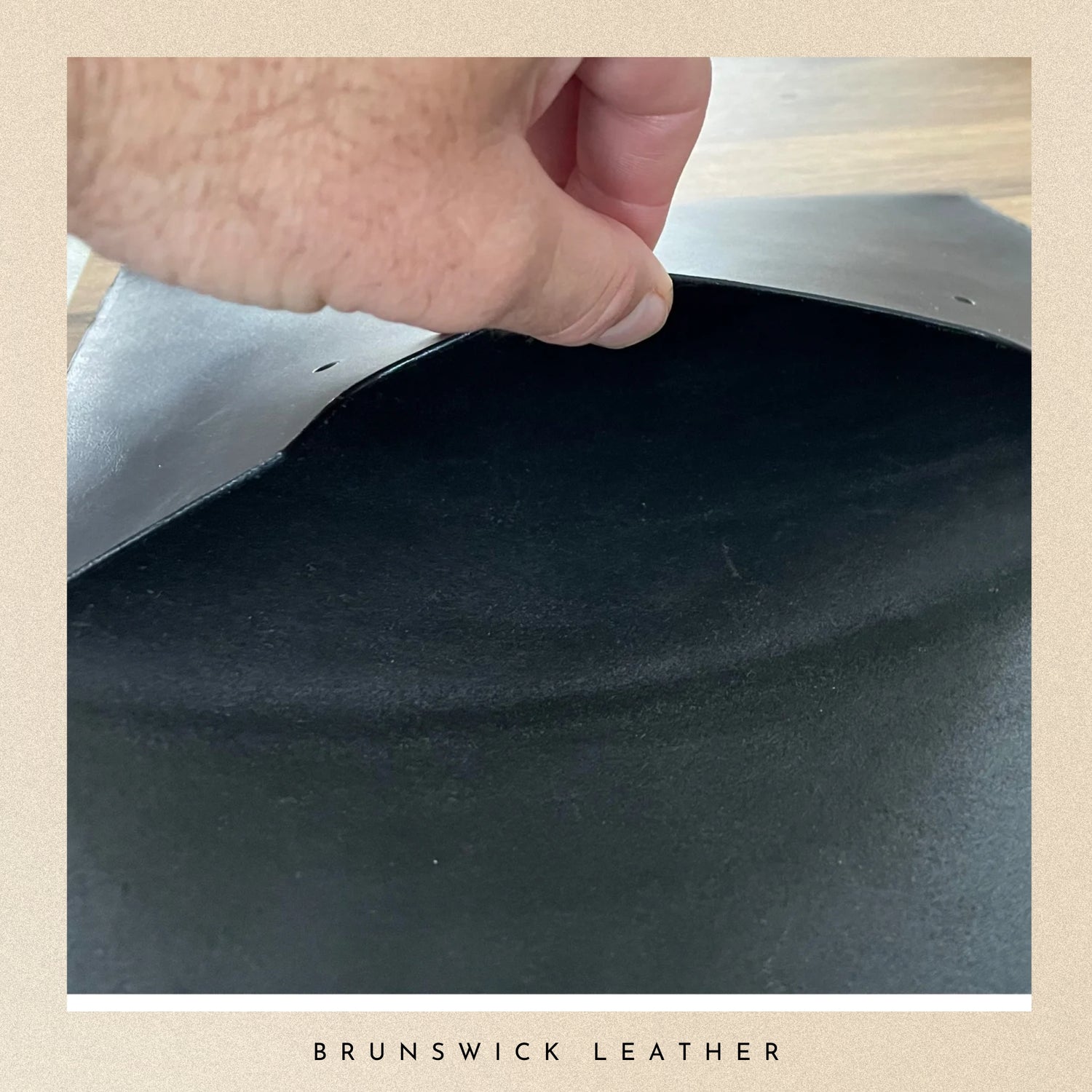 Close-up of a hand holding a piece of black leather with 'Brunswick Leather' branding.
