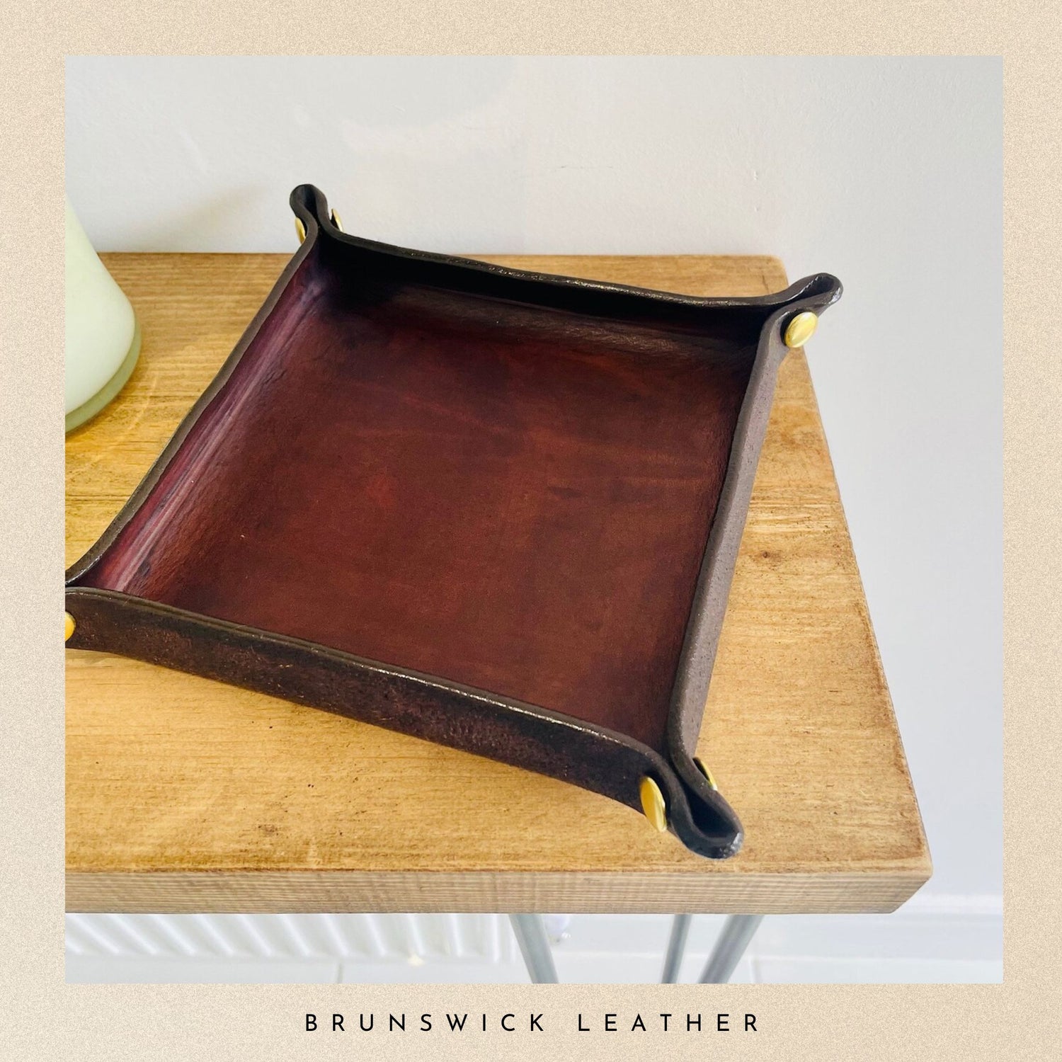 Brown leather tray with gold accents on a wooden surface, branded 'Brunswick Leather'.