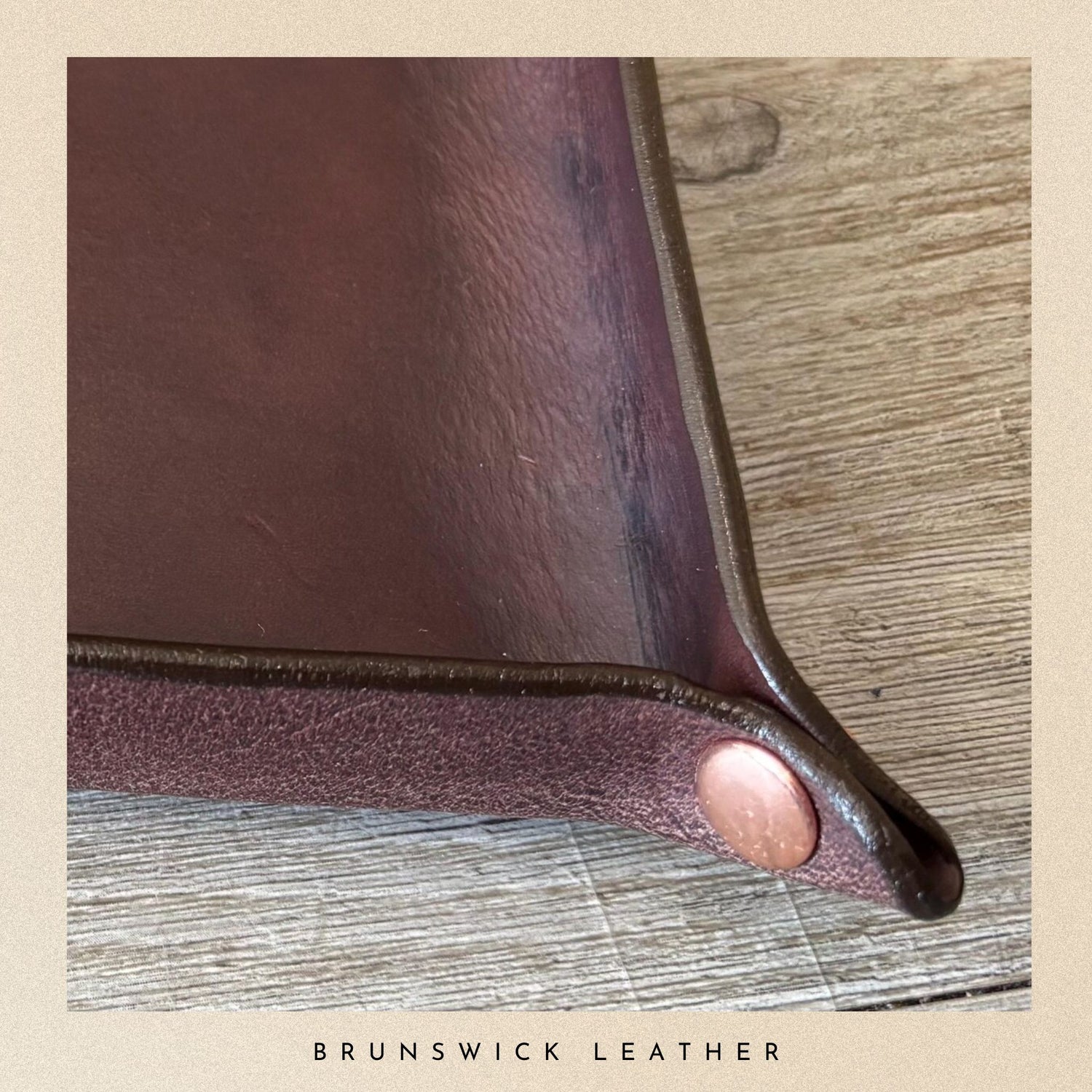 Close-up of a brown leather product with a metallic accent on a wooden surface, branded 'Brunswick Leather'.