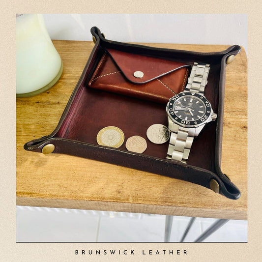 Leather tray with a watch, coins, and wallet on a wooden surface, branded 'Brunswick Leather'.