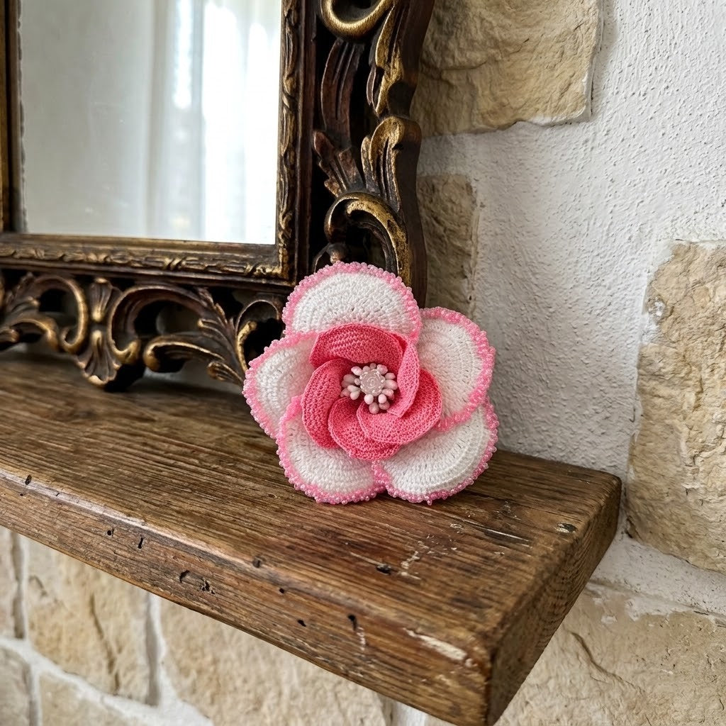 A handmade fabric flower brooch in pink and white, styled on a rustic wooden mantelpiece next to an ornate mirror.