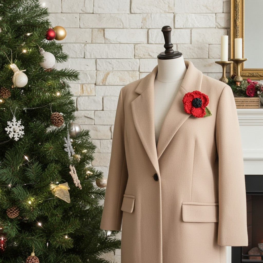 A beige wool coat displayed on a mannequin torso, styled with a red poppy brooch, set against a Christmas fireplace scene with a decorated Christmas tree and white brick wall.