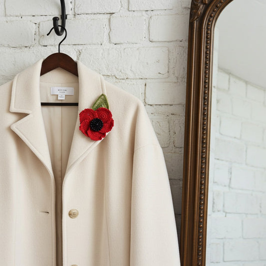 Beige coat with a red remembrance poppy on a hanger against a white brick wall.