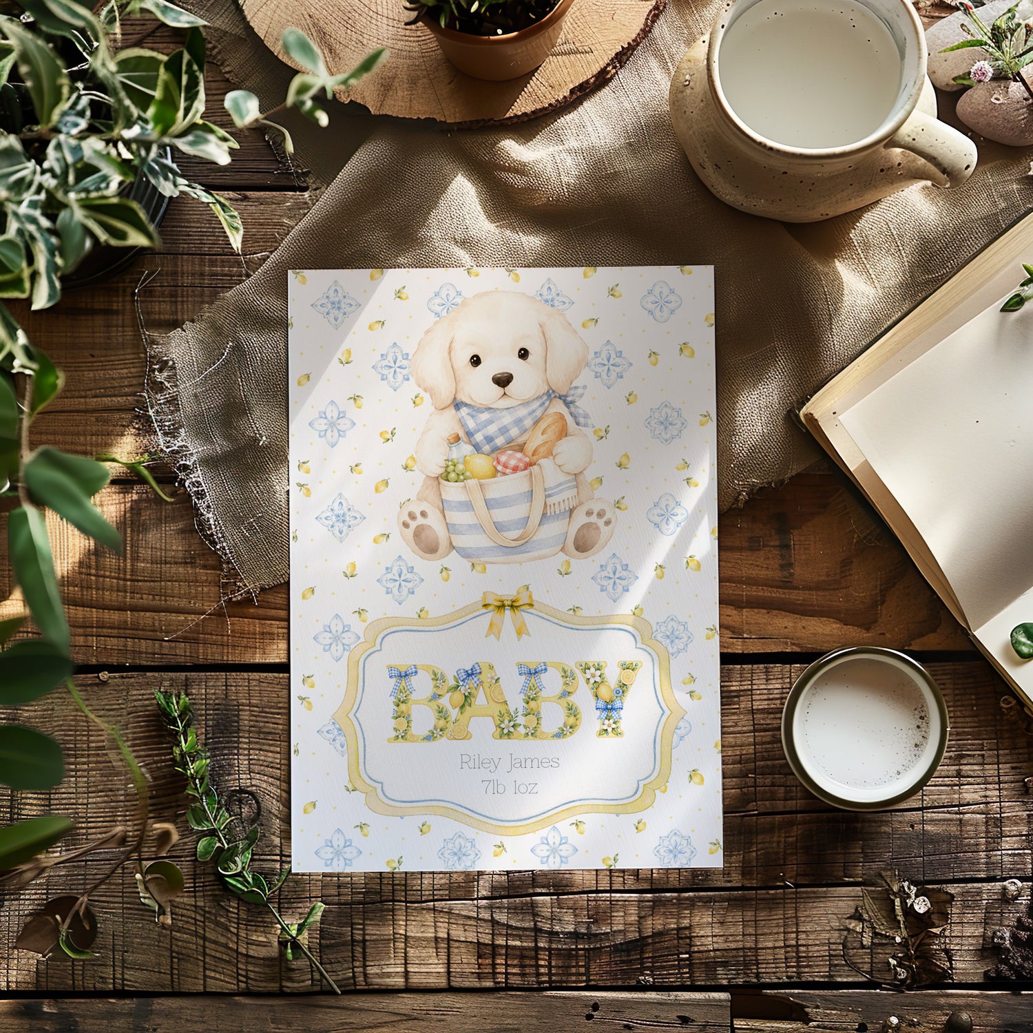 A baby card titled BABY with the baby's name and weight featuring an illustration of a puppy in a basket, styled in a flat-lay on a rustic wooden table with a mug, book, and greenery.