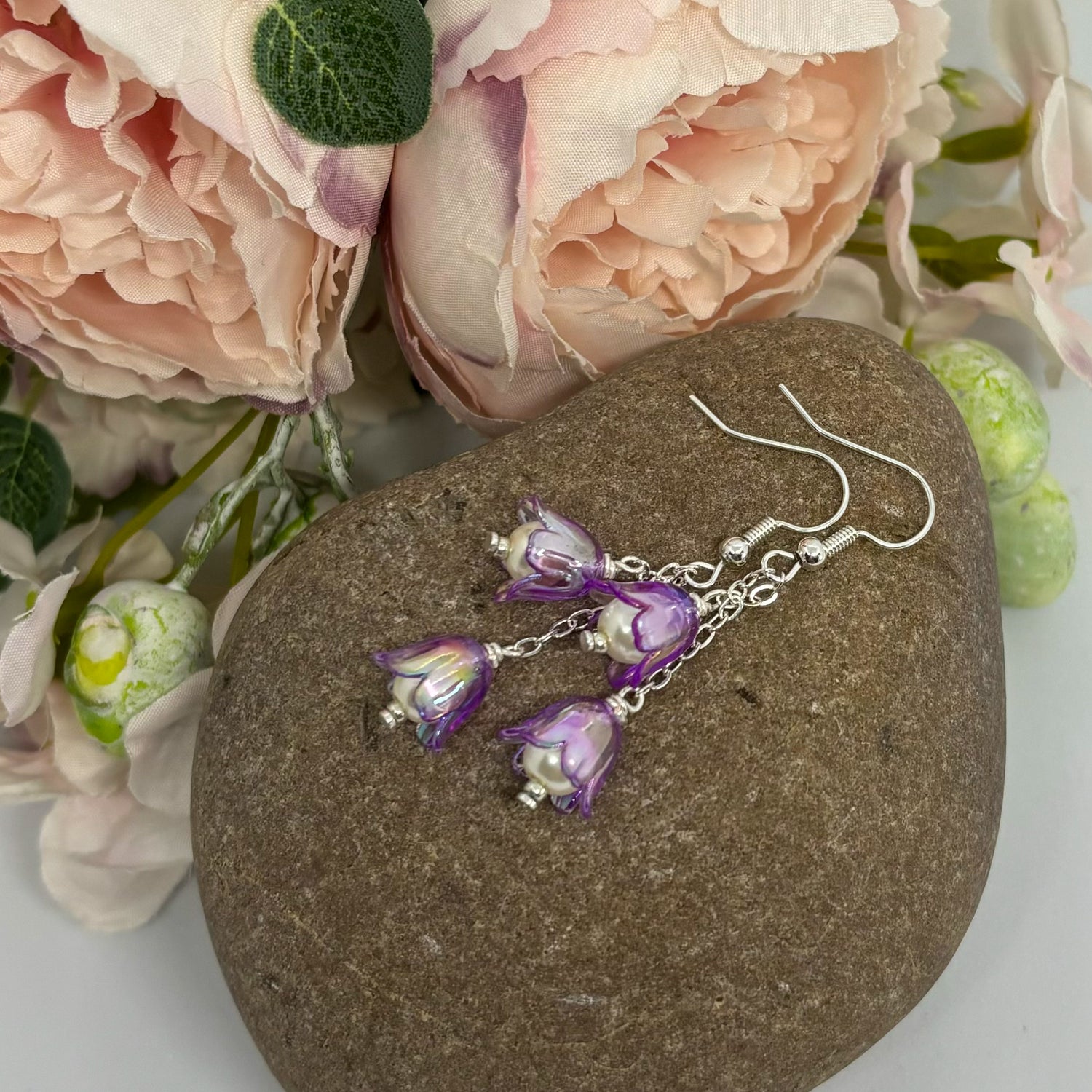 purple floral earrings with silver hooks on a stone