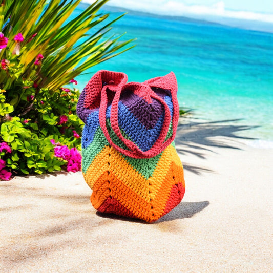 Colorful crocheted bag on a sandy beach with ocean and plants in the background