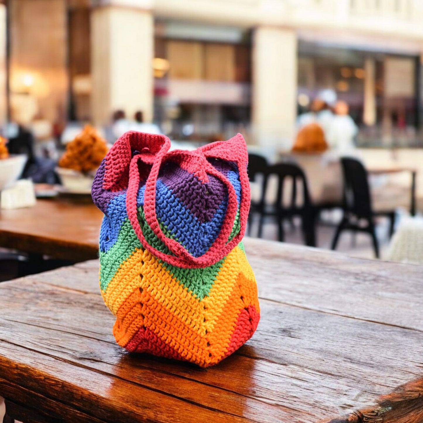 Colorful crocheted bag on a wooden table with a blurred restaurant background