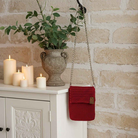 Red knitted bag hanging on a brick wall with candles and a plant in the background.