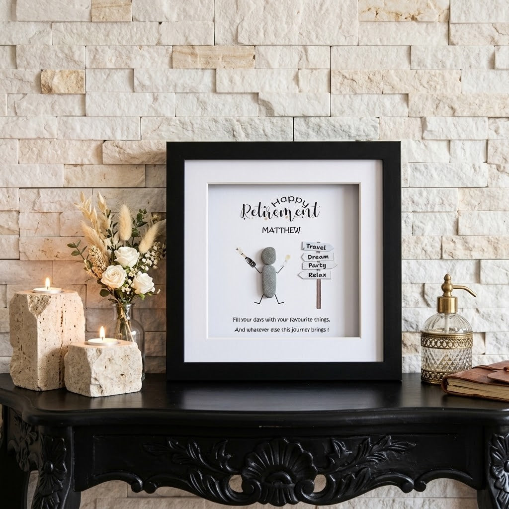 A framed personalised retirement gift displayed on a black carved console table against a light stone brick wall. The black frame contains a white background with a small stick-figure style character and the text 'HAPPY Retirement MATTHEW!' 